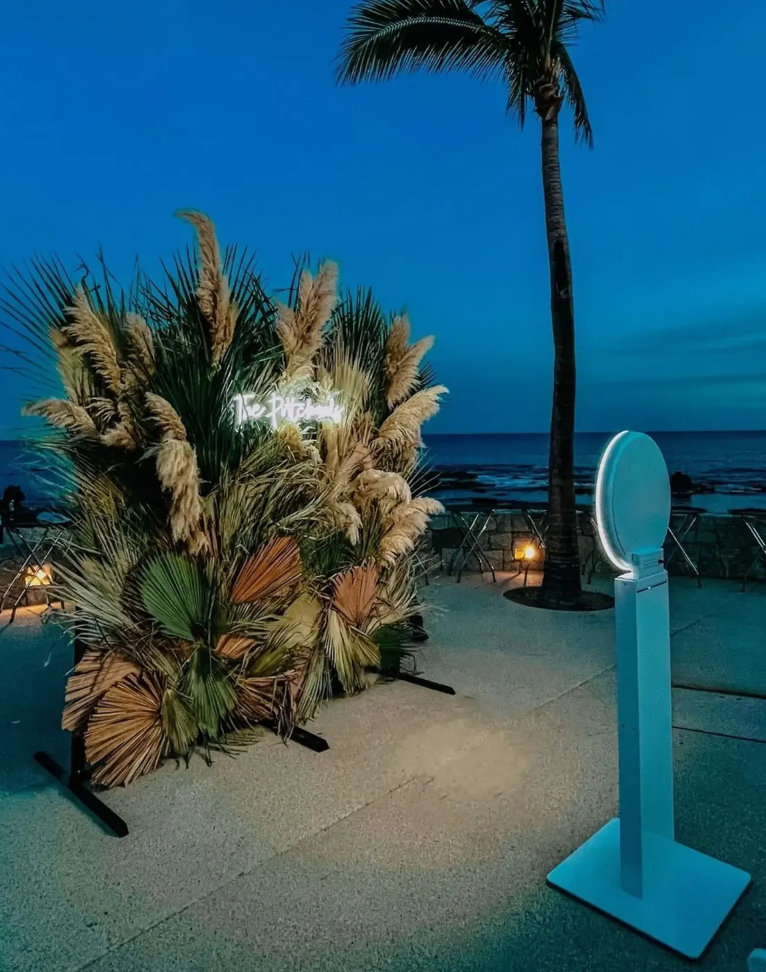 Ring light photo booth beside a pampas grass backdrop at an oceanfront wedding