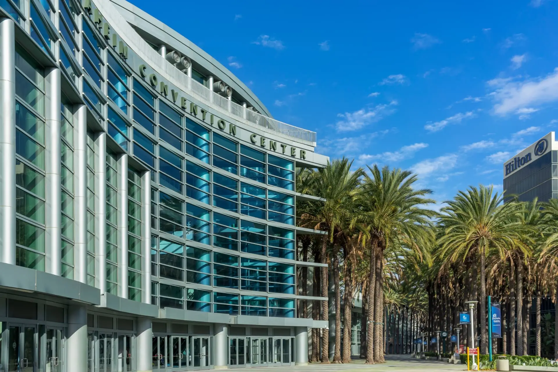 The Anaheim Convention Center glass facade with palm trees along the entry plaza