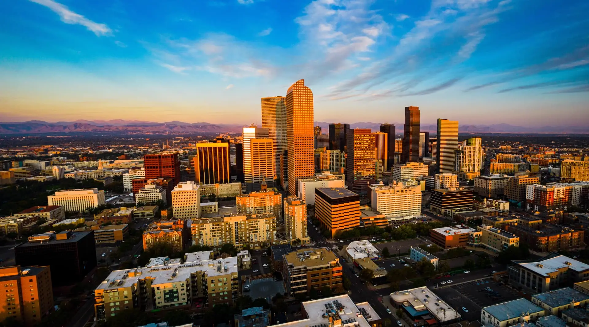 Aerial view of downtown Denver at sunset with the Rocky Mountains behind