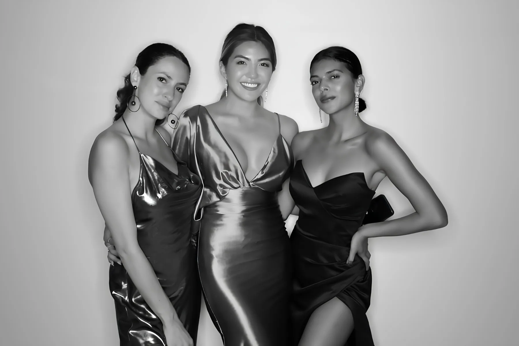 Three women in elegant satin gowns posing in the Glam Booth — black and white editorial portrait