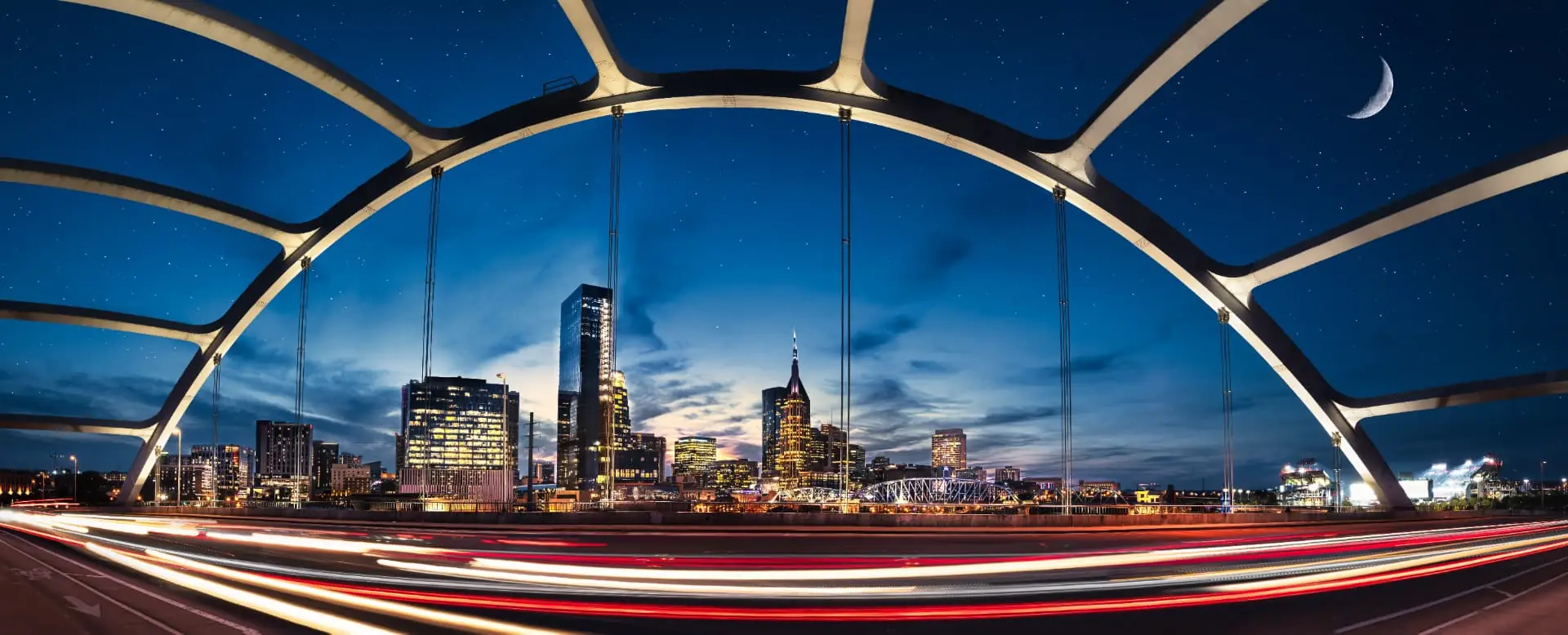 The Nashville skyline at blue hour framed by a lit pedestrian bridge arch