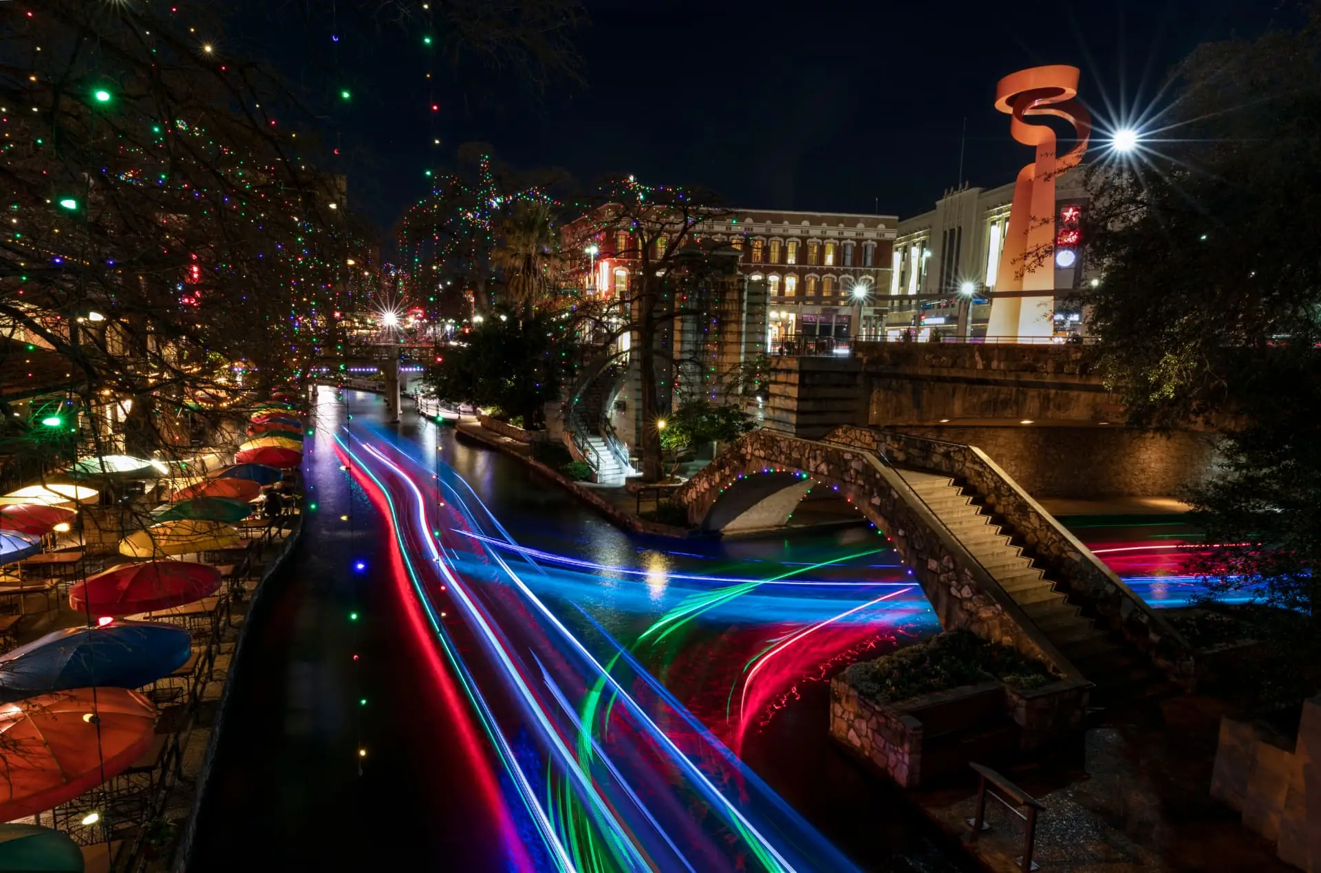 The San Antonio River Walk at night lit with holiday lights and boat light trails