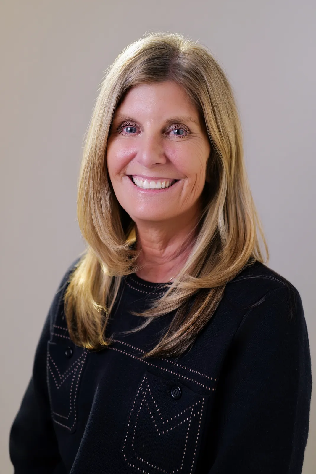 Studio headshot of a smiling blonde woman in a black sweater on a gray backdrop