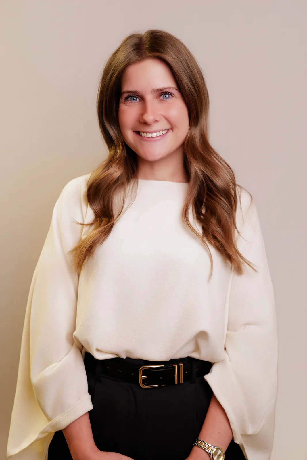 Studio headshot of a smiling brunette woman in a cream blouse on a beige backdrop